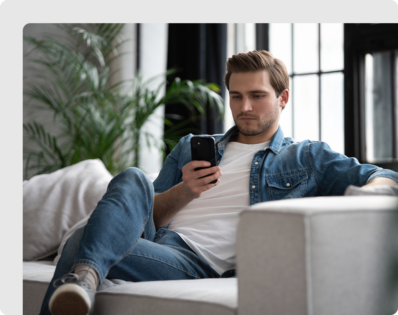 Man lounging on a sofa while checking his smartphone
