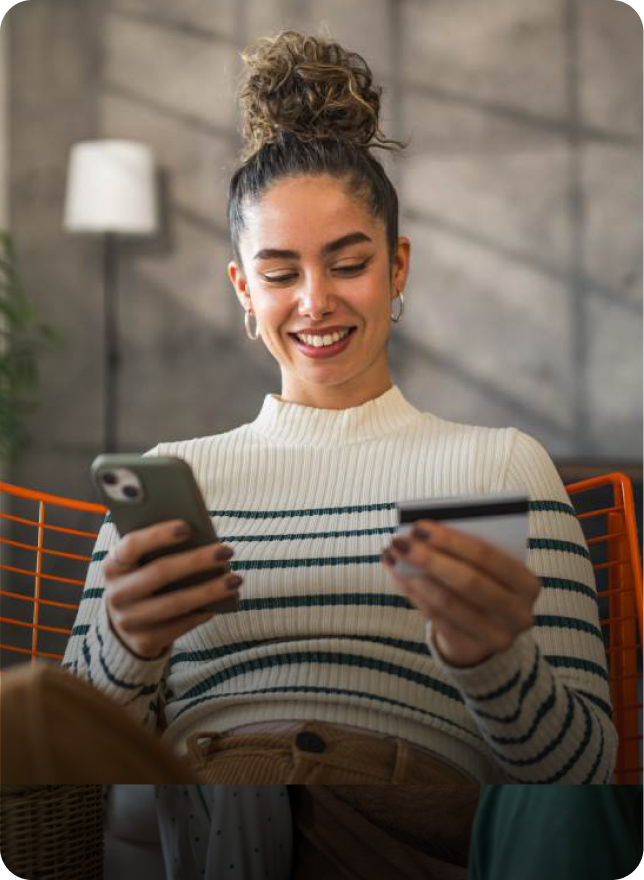 Woman holding a phone and credit card, smiling while making a purchase