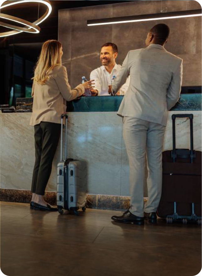 Two travelers checking in at a hotel front desk with suitcases