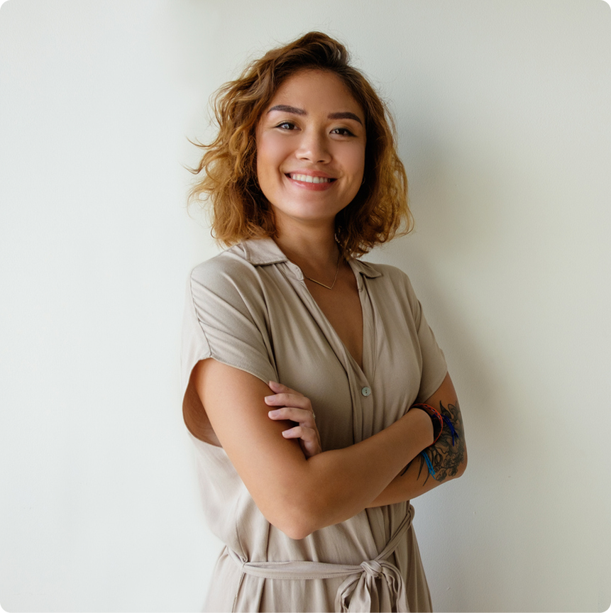 Confident young woman with short curly hair smiling, arms crossed against a white wall